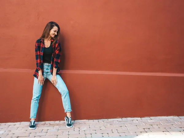 美丽的微笑模型的肖像 穿着夏季嬉皮士格子衬衫和牛仔裤的女性 一个时髦的女孩在街上靠墙站着 在户外玩乐的有趣而积极的女人 — 图库照片