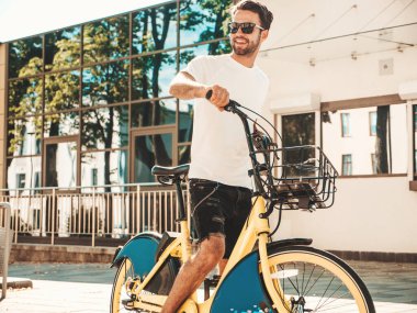 Yakışıklı, gülümseyen stil sahibi Lambersex modelinin portresi. Beyaz tişört giyen adam. Moda erkeği, arka planda güneş gözlüklü bisiklet sürüyor.