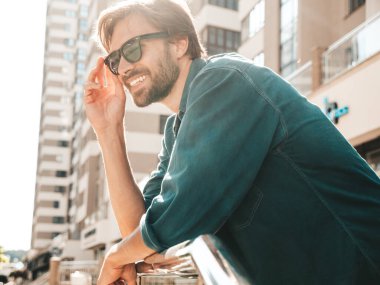 Yakışıklı, gülümseyen stil sahibi Lambersex modelinin portresi. Yeşil tişörtlü adam. Moda erkek gökdelenin arkasında güneş gözlükleriyle poz veriyor.