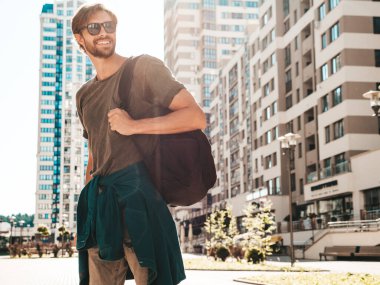 Yakışıklı, gülümseyen stil sahibi Lambersex modelinin portresi. Yeşil tişörtlü adam. Moda erkeği güneş gözlükleriyle gökdelende poz veriyor. Gün batımında dışarıda yürüyor. 