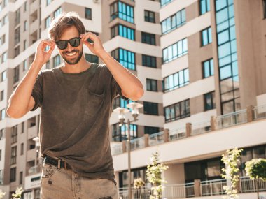 Yakışıklı, gülümseyen stil sahibi Lambersex modelinin portresi. Yeşil tişörtlü adam. Moda erkeği güneş gözlükleriyle gökdelende poz veriyor. Gün batımında dışarıda yürüyor. 