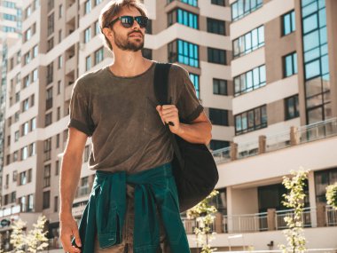 Yakışıklı, gülümseyen stil sahibi Lambersex modelinin portresi. Yeşil tişörtlü adam. Moda erkeği güneş gözlükleriyle gökdelende poz veriyor. Gün batımında dışarıda yürüyor. 