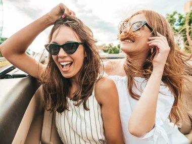 Üstü açık arabadaki iki güzel ve gülümseyen hippi kızın portresi. Cabriolet kullanan kaygısız seksi kadınlar. Pozitif modeller güneş gözlükleriyle geziyor ve eğleniyorlar.