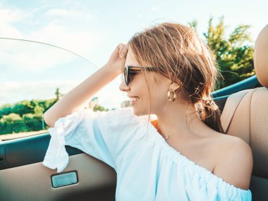 Üstü açık arabadaki güzel ve gülümseyen hippi kız portresi. Cabriolet kullanan kaygısız seksi kadın. Pozitif model sürüş ve güneş gözlükleriyle eğlenme