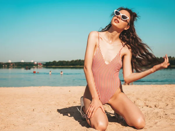 青い海と空の背景にポーズサングラスで若い美しいセクシーなヒップスター女性 夏の水着水着のトレンドの女の子 正の女性はクレイジー行きます 面白いモデルは砂の上に座って — ストック写真