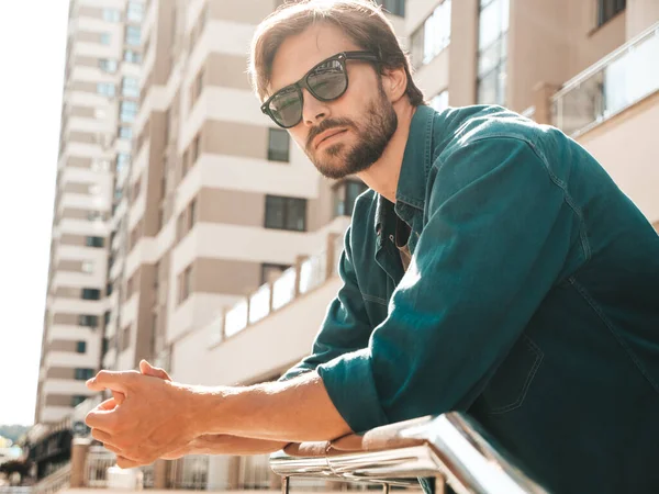 Yakışıklı, kendine güvenen, stil sahibi, Lambersex mankeni portresi. Yeşil tişörtlü adam. Moda erkek gökdelenin arkasında güneş gözlükleriyle poz veriyor.