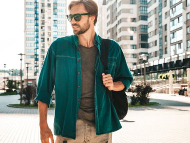 Yakışıklı, şık bir hipster Lambersex modelinin portresi. Yeşil gömlekli bir adam. Moda erkeği güneş gözlükleriyle gökdelende poz veriyor. Gün batımında dışarıda yürüyor. 