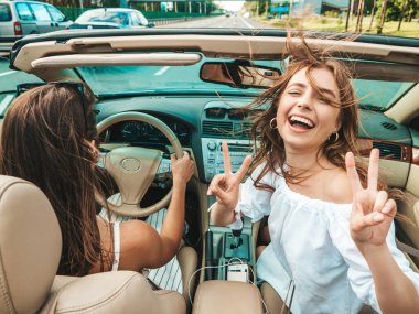 Üstü açık arabadaki iki güzel ve gülümseyen hippi kızın portresi. Cabriolet kullanan kaygısız seksi kadınlar. Pozitif modeller güneş gözlükleriyle geziyor ve eğleniyorlar.