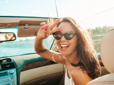 Üstü açık arabadaki güzel ve gülümseyen hippi kız portresi. Cabriolet kullanan kaygısız seksi kadın. Gün batımında güneş gözlüğüyle gezmek ve eğlenmek