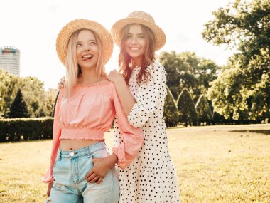 İki genç, güzel, gülümseyen yeniyetme kadın, modaya uygun bir yaz elbisesi içinde. Parkta şapkalarla poz veren kaygısız seksi kadınlar. Pozitif modeller gün batımında eğleniyor ve sarılıyorlar.