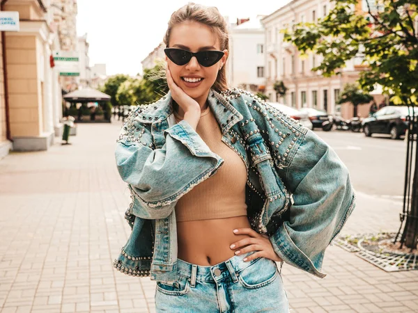 Hipster kot ceket giymiş güzel gülümseyen bir modelin portresi. Sokakta poz veren modaya uygun bir kız. Komik ve pozitif kadın güneş gözlükleriyle eğleniyor.