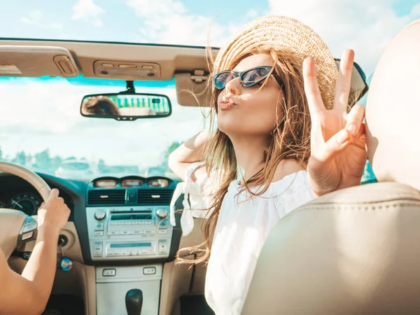 Üstü açık arabadaki iki güzel ve gülümseyen hippi kızın portresi. Cabriolet kullanan kaygısız seksi kadınlar. Pozitif modeller güneş gözlükleriyle geziyor ve eğleniyorlar.