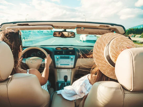 Üstü açık arabadaki iki güzel ve gülümseyen hippi kızın portresi. Cabriolet kullanan kaygısız seksi kadınlar. Pozitif modeller güneş gözlükleriyle geziyor ve eğleniyorlar.