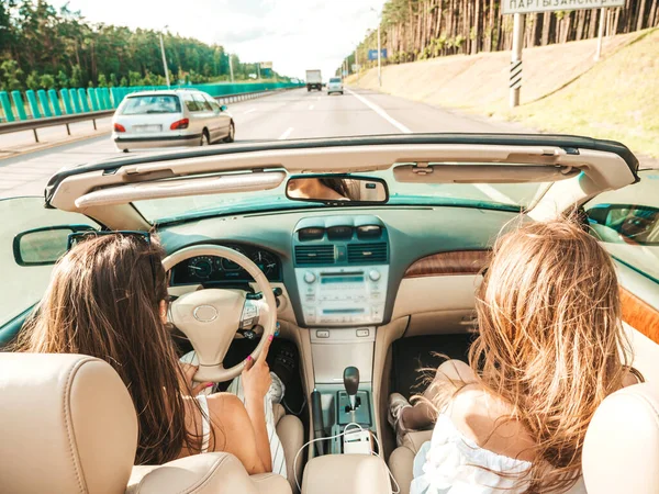 Üstü açık arabadaki iki güzel ve gülümseyen hippi kızın portresi. Cabriolet kullanan kaygısız seksi kadınlar. Pozitif modeller güneş gözlükleriyle geziyor ve eğleniyorlar.