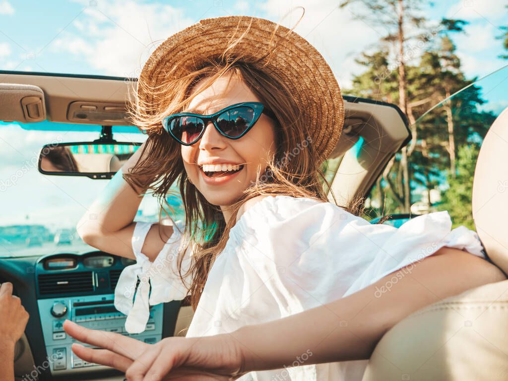 Portrait of two young beautiful and smiling hipster girls in convertible car. Sexy carefree women driving cabriolet. Positive models riding and having fun in sunglasses