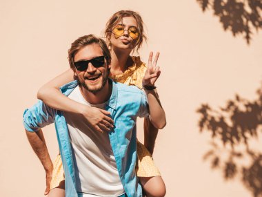 Gülümseyen güzel kız ve yakışıklı erkek arkadaşının portresi. Gündelik yazlık elbiseli kadın ve kot pantolonlu erkek. Mutlu, neşeli bir aile. Kadın duvarın yanında eğleniyor.