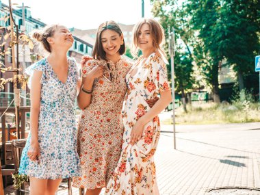 Üç güzel gülümseyen yeniyetme kız şık yaz kıyafetleri içinde. Sokakta poz veren kaygısız kadınlar. Modeller eğleniyor ve sarılıyorlar.