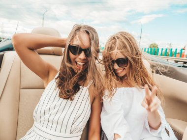Üstü açık arabadaki iki güzel ve gülümseyen hippi kızın portresi. Cabriolet kullanan kaygısız seksi kadınlar. Pozitif modeller güneş gözlükleriyle geziyor ve eğleniyorlar.