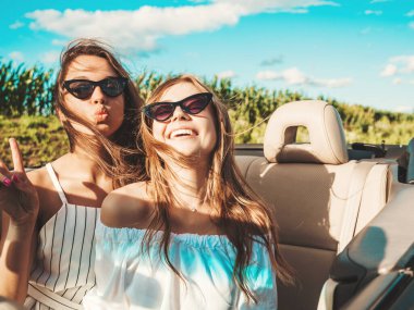 Üstü açık arabadaki iki güzel ve gülümseyen hippi kızın portresi. Cabriolet kullanan kaygısız seksi kadınlar. Pozitif modeller güneş gözlükleriyle geziyor ve eğleniyorlar.