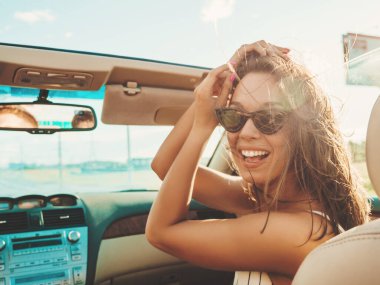 Üstü açık arabadaki güzel ve gülümseyen hippi kız portresi. Cabriolet kullanan kaygısız seksi kadın. Gün batımında güneş gözlüğüyle gezmek ve eğlenmek