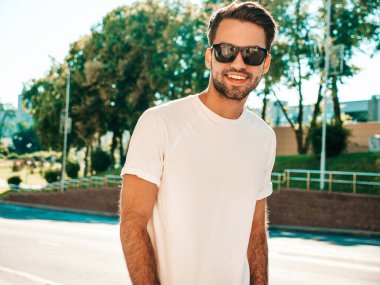 Yakışıklı, gülümseyen stil sahibi Lambersex modelinin portresi. Beyaz tişört giyen adam. Sokakta güneş gözlükleriyle poz veren modacı erkek.