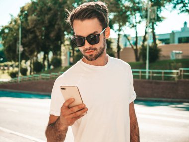 Yakışıklı, şık, havalı, lamberseksüel bir model. Beyaz tişört giymiş bir adam. Sokakta poz veren bir erkek. Cep telefonunda tutuyor, kaydırıyor ve mesaj atıyor. Akıllı telefondan mesaj yazar