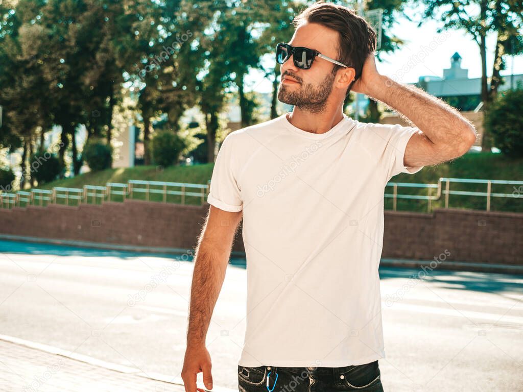 Portrait of handsome smiling stylish hipster lambersexual model.Man dressed in white T-shirt. Fashion male posing on the street background in sunglasses