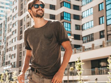 Yakışıklı, gülümseyen stil sahibi Lambersex modelinin portresi. Yeşil tişörtlü adam. Moda erkek gökdelen arka planında güneş gözlükleriyle sokakta poz veriyor. Gün batımında dışarıda. 