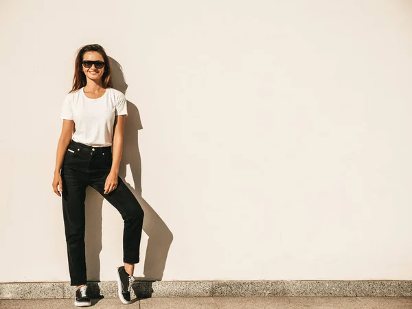 戴着太阳镜的漂亮模特的画像 穿着夏季嬉皮士白色T恤和牛仔裤的女性 在街上靠墙摆姿势的时髦女人 — 图库照片