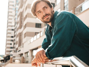 Yakışıklı, gülümseyen stil sahibi Lambersex modelinin portresi. Yeşil tişörtlü adam. Moda erkek gökdelen arka planında sokakta poz veriyor