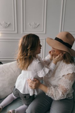 Genç anne ve küçük gülümseyen anaokulu kızı kanepede oturur sırlarını paylaşır dedikodu yapar, anne heyecanlı küçük kız kulağına fısıldar sohbet eder.