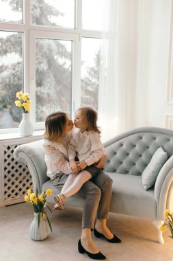 Neşeli yetişkin anne, küçük kızıyla kanepede gülüşüyor, neşeli genç anne, sevimli çocuk kızla eğleniyor, kahkaha atıyor, komik aile hayatı yaşıyor, kanepeye oturup rahatlıyor.