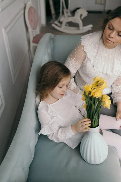 Smiling young mother and little daughter cuddle have fun sitting on couch at home, overjoyed mom or nanny playing with small preschooler girl child tickle and laugh, enjoy leisure weekend at home