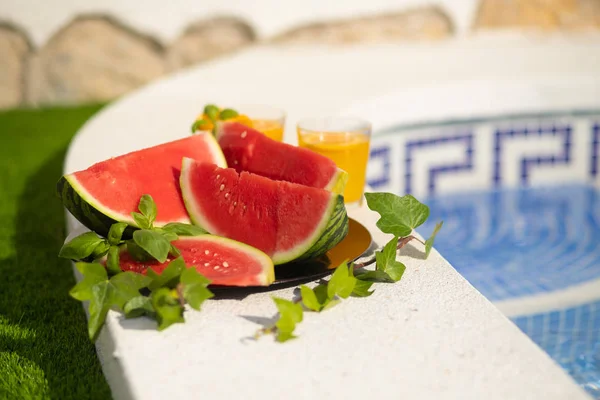 Concepto tropical de vacaciones de verano. Zumo de naranja fresco y jugo de sandía y piña en el borde de una piscina . — Foto de Stock