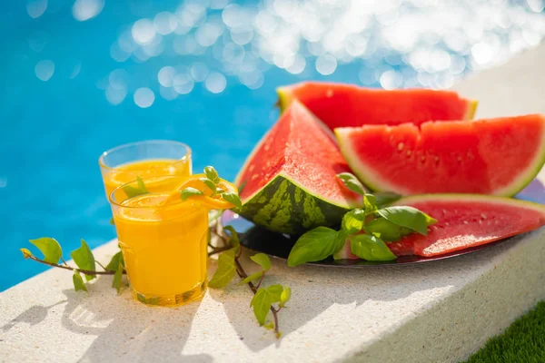 Conceito tropical de férias de verão. Sumo de laranja fresco e suco de melancia e abacaxi na borda de uma piscina . — Fotografia de Stock