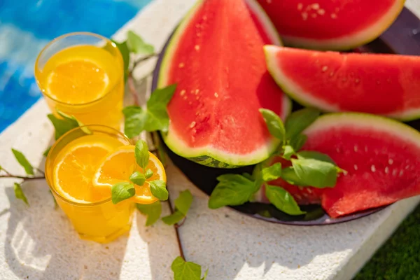 Concepto tropical de vacaciones de verano. Zumo de naranja fresco y jugo de sandía y piña en el borde de una piscina . — Foto de Stock