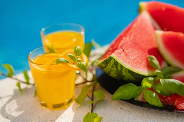 Conceito tropical de férias de verão. Sumo de laranja fresco e suco de melancia e abacaxi na borda de uma piscina . — Fotografia de Stock