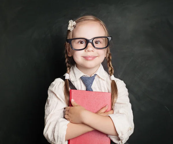 本児は 小さな女子高生制服本を押しながら緑のチョーク ボード背景に笑みを浮かべてします 子供の学習と教育の概念に戻る — ストック写真