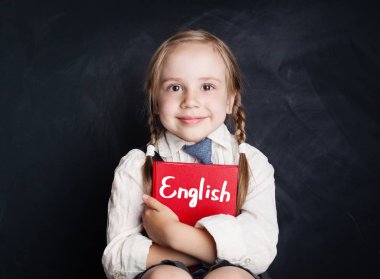 İngilizce dil kavram. Şirin çocuk öğrenci sınıf tahta arka plan karşı oturuyor ve gülümseyen kitap ile