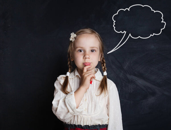 Thinking little girl against speech clouds chalk drawing on blackboard background. Cute pensive child portrait