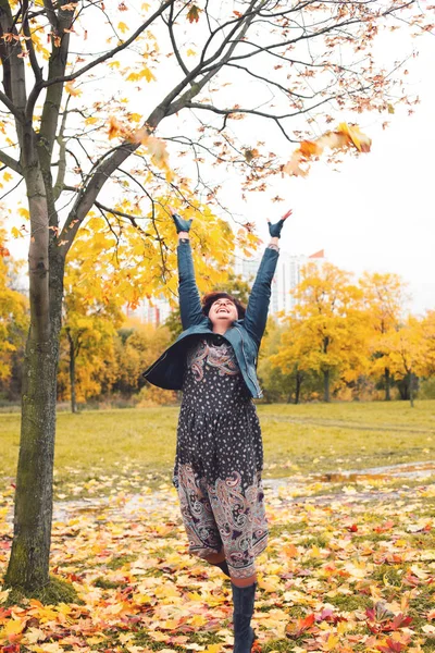 Happy woman throws up autumn leaves outdoors