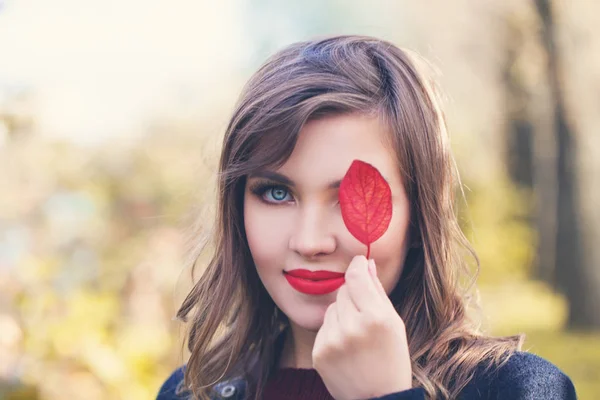 秋の公園で赤い紅葉の葉を保持している赤い唇メイクと秋の女性の肖像画 — ストック写真