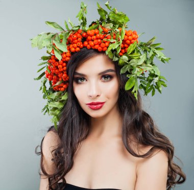 Genç esmer kadın moda model sağlıklı kıvırcık saç modeli, makyaj ve kırmızı meyveler ve saç yeşil yaprakları ile