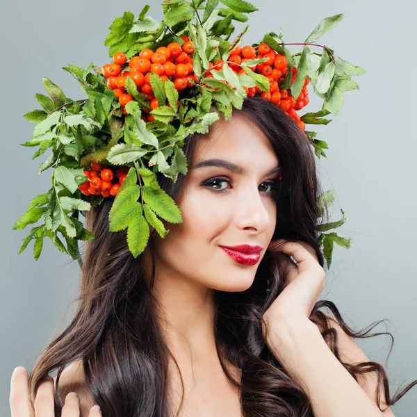 Portrait of young happy woman with makeup, wavy hair and red berries and green leaves on head