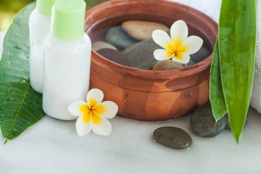 Spa ya da sağlık ayarıyla tropik çiçekler, su, havlu ve krem tüp kase. Vücut bakımı ve spa konsept açık havada