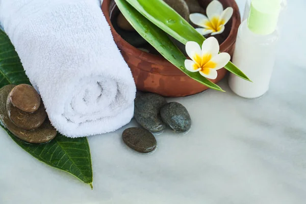 Towel, flowers, green leaves and cosmetics on white marble background outdoors