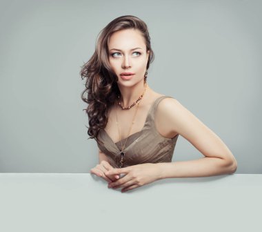 Kıvırcık saç modeli, makyaj ve yukarıya bakıp beyaz arka plan üzerinde oturan fashionable takı glamourous kadınla. Genç kadın modeli moda portre mükemmel