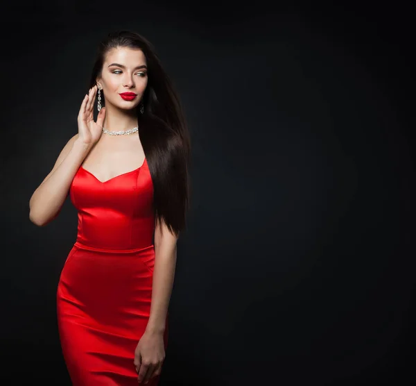 Glamorous woman wearing red dress. Sexy model with red lips makeup and diamond jewelry on black background with copy space