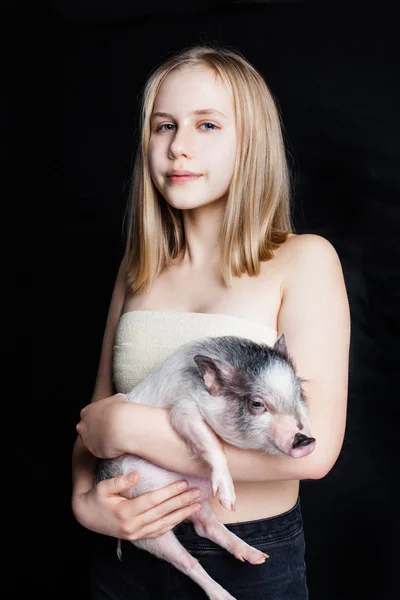 かわいいティーンエイ ジャーの女の子が黒の背景に豚を保持している肖像画 — ストック写真