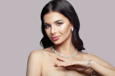 Makyaj ve elmas kolye, bileklik ve küpe pembe bir arka plan üzerinde genç gülümseyen kadın